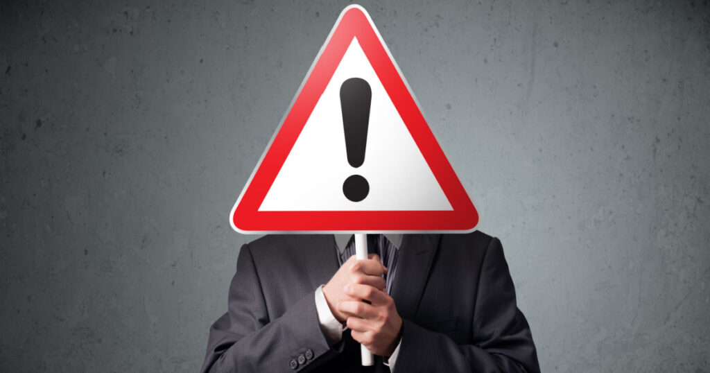 Businessman holding a red traffic triangle warning sign in front of his head
