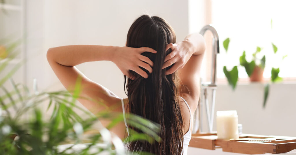 Young woman applying coconut oil onto her hair in bathroom
