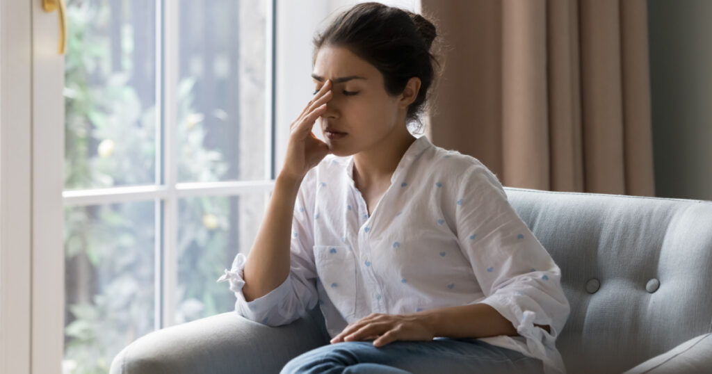 Depressed frustrated young Indian woman suffering from headache, migraine, touching face, head with closed eyes, feeling stressed, sick, tired, thinking over bad news, problems, crisis