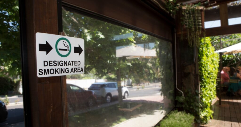 Designated smoking area sign pointing to open garden area. Hotel smoking policies concept