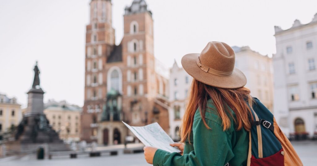 Attractive young female tourist is exploring new city. Redhead girl holding a paper map on Market Square in Krakow. Traveling Europe in autumn. St. Marys Basilica
