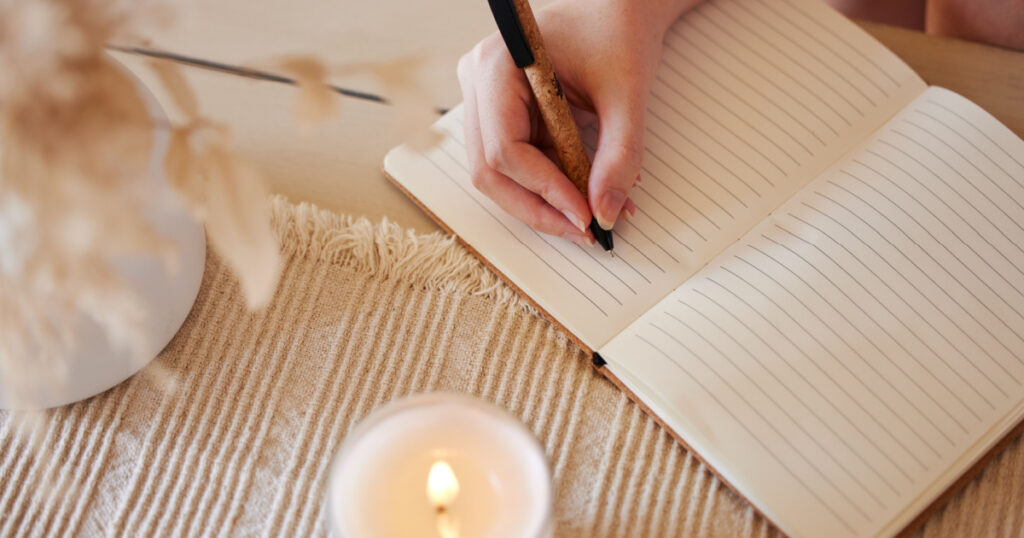 Hand, candle and woman writing in journal with top view for calm, peace mindset and relax morning routine in home. Hands, notebook and diary planning goals, idea vision or creative writer lifestyle