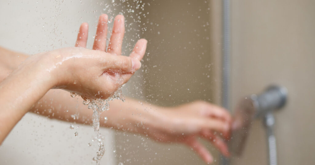 A woman uses hand to measure the water temperature from a water heater before taking a shower
