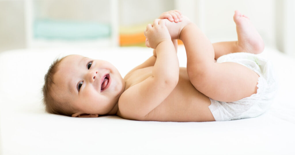 happy baby lying on white sheet and holding his legs