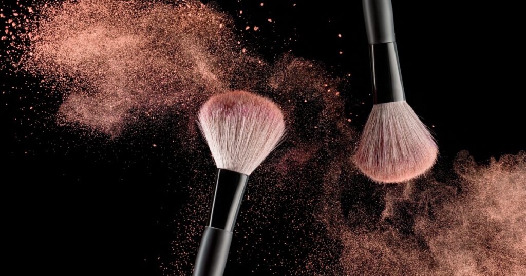 Make-up brush with pink powder explosion on black background
