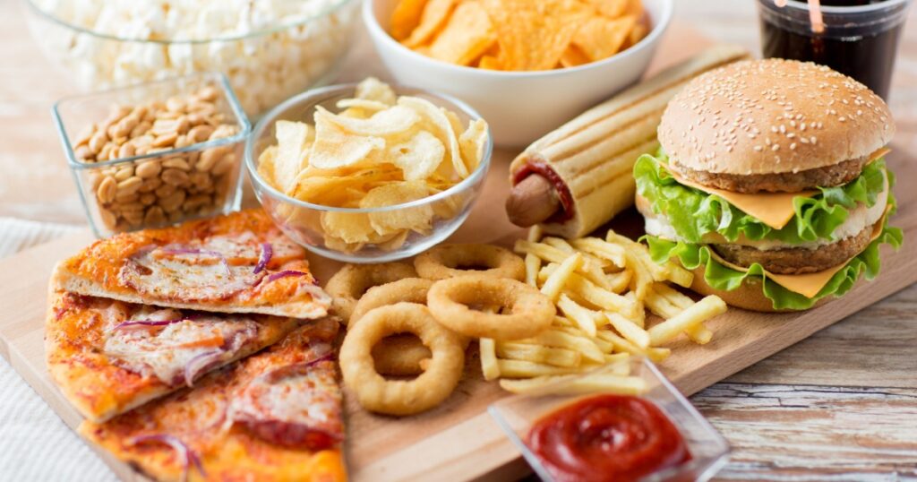 fast food and unhealthy eating concept - close up of fast food snacks and cola drink on wooden table