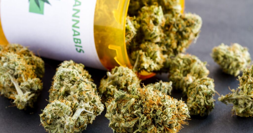 Close up of medical marijuana buds spilling out of prescription bottle with label on black background