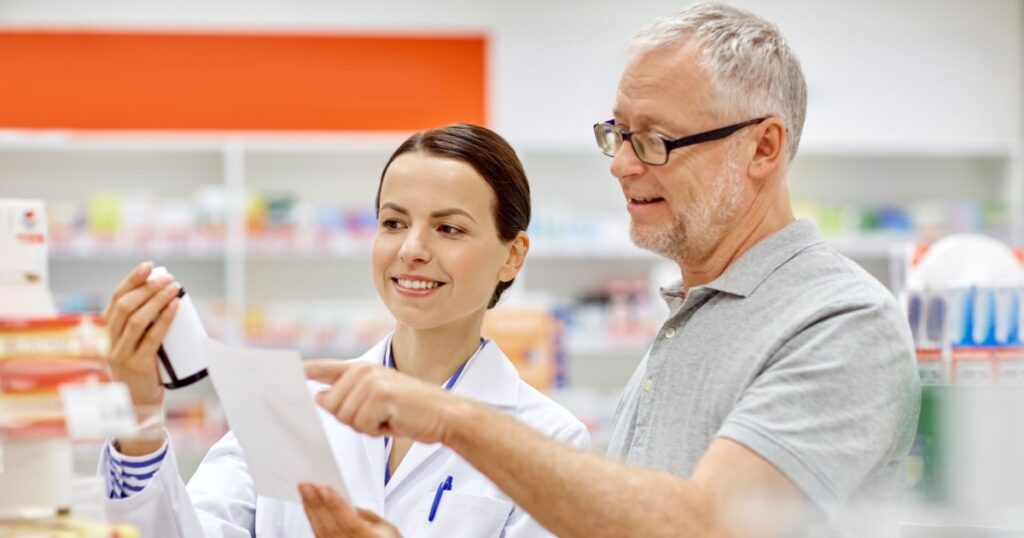 medicine, pharmaceutics, health care and people concept - happy pharmacist and senior man customer with drug and prescription at drugstore