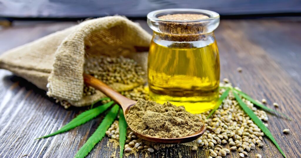 Flour hemp in a wooden spoon, seed in a bag and on the table, oil in a glass jar, cannabis leaves on the background of wooden boards