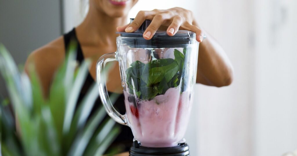 Woman blending spinach, berries, bananas and almond milk to make a healthy green smoothie