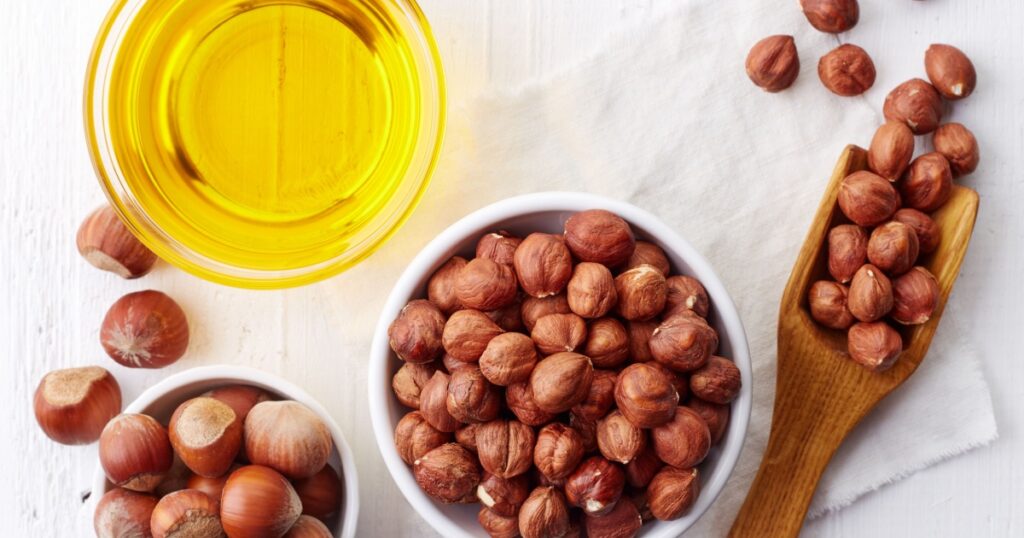 Bowl of hazelnut oil and hazelnuts on white wooden background. From top view