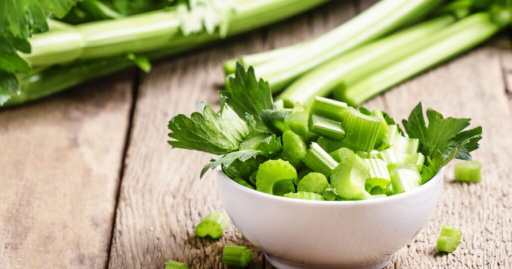 Fresh sliced celery in a white bowl on a vintage wooden background, selective focus
