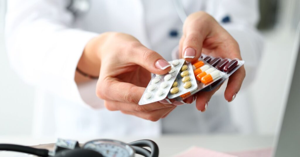 Female doctor hand holding pack of different tablet blisters at workplace closeup. Panacea, life save service, prescribe medicament, legal drug store, disease healing, blood pressure concept