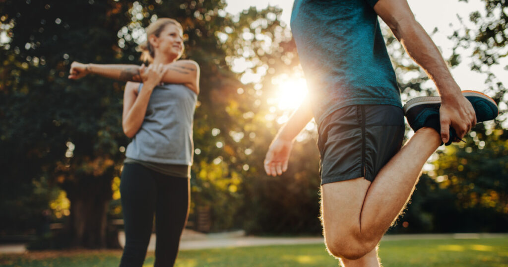 Shot of young man and woman stretching in the park. Young couple warming up in morning.