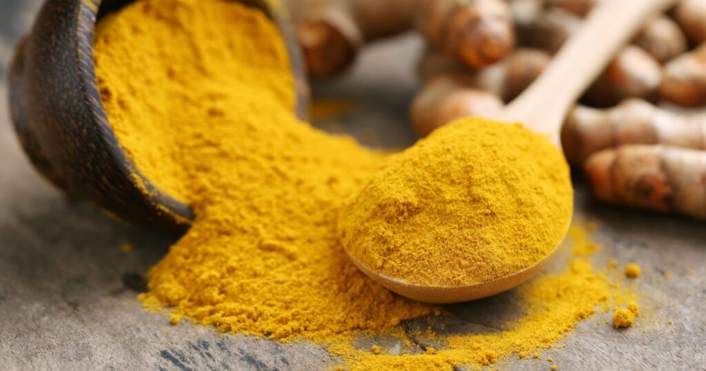Turmeric powder and fresh turmeric on wooden background.