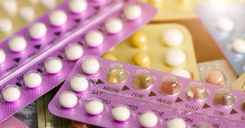 Oral contraceptive pill on pharmacy counter with colorful pills strips background.