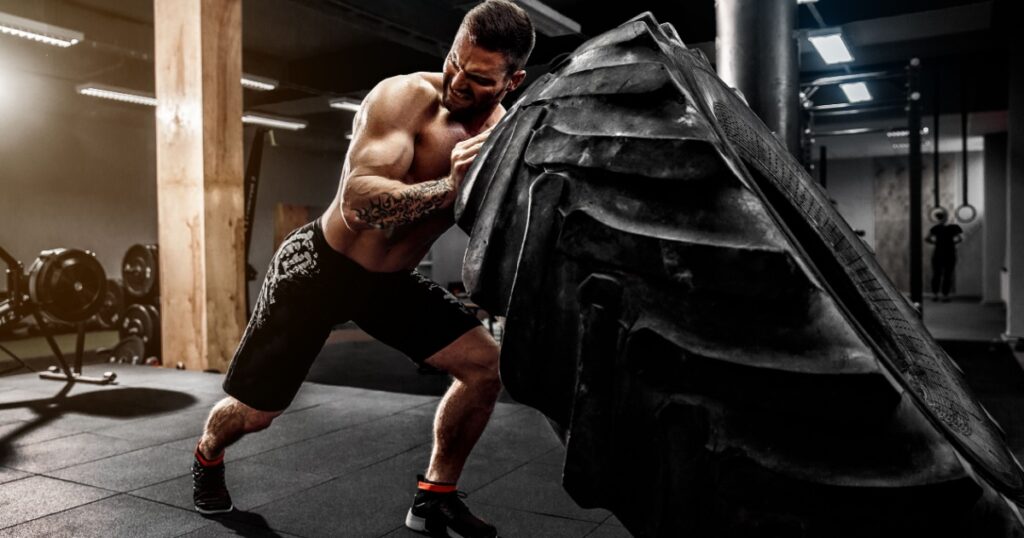Shirtless man flipping heavy tire at gym