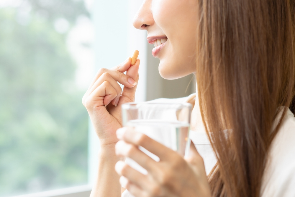 Dietary supplement, asian young woman, girl hand holding orange medical pill, take or eat vitamin C, D for treatment for skin, hair and nail strengthen with glass of pure water at home, healthcare.