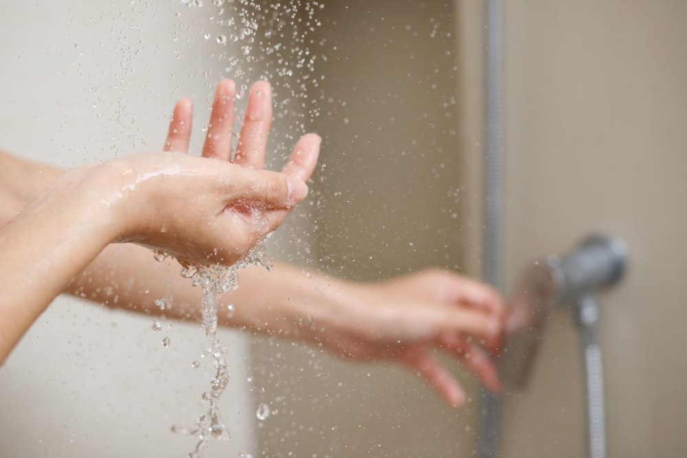 A woman uses hand to measure the water temperature from a water heater before taking a shower

