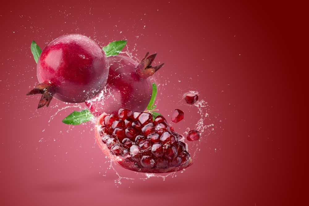 Creative layout made from Fresh pomegranate fruit and water Splashing on red background.
