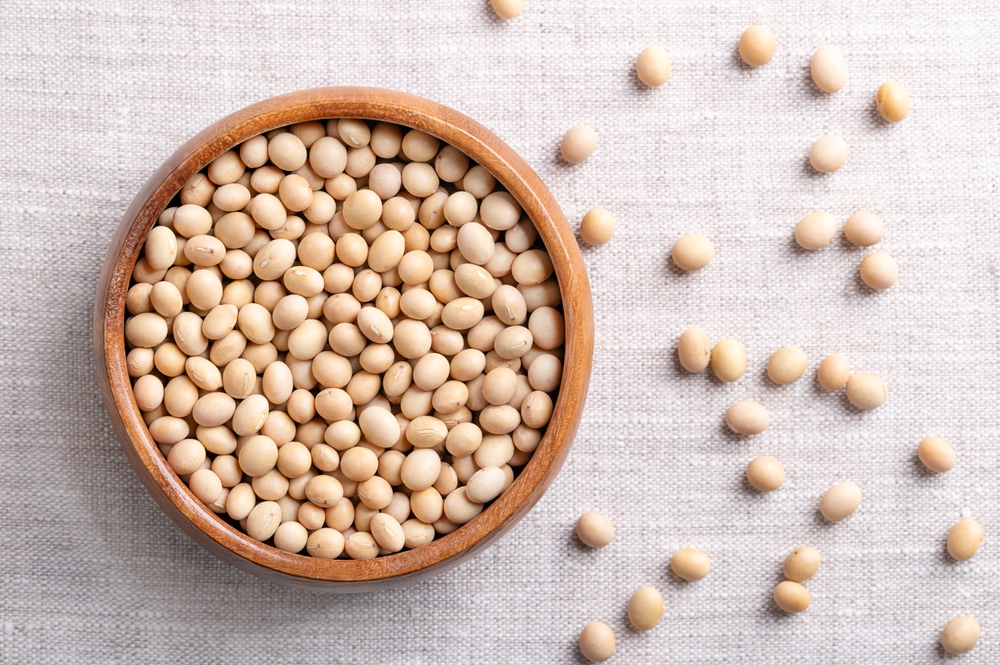 Dried soybeans, also soy beans or soya beans in a wooden bowl on linen fabric. Whole and raw seeds of the legume and oilseed Glycine max, with a very high protein and oil content. Close-up from above.
