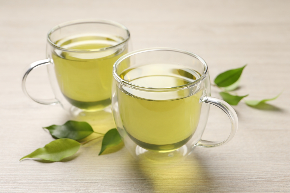 Refreshing green tea in cups and leaves on wooden table, closeup
