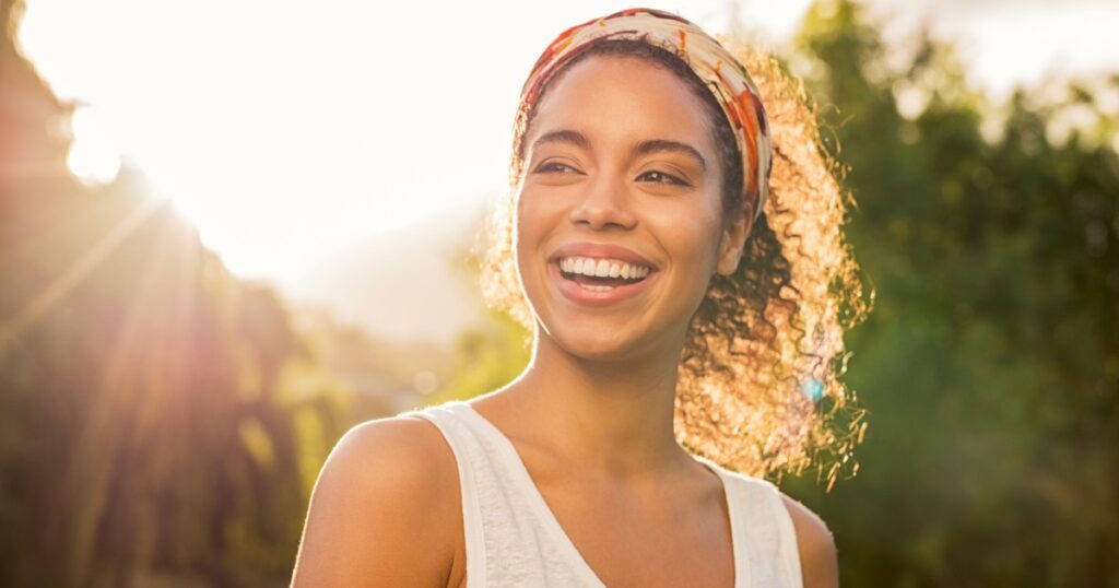 Portrait of beautiful african american woman smiling and looking away at park during sunset. Outdoor portrait of a smiling black girl. Happy cheerful girl laughing at park with colored hair band.