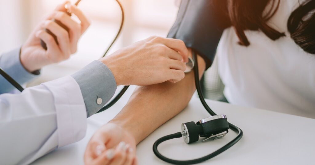 Doctor using sphygmomanometer with stethoscope checking blood pressure to a patient in the hospital.