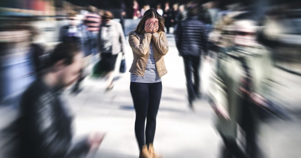 Panic attack in public place. Woman having panic disorder in city. Psychology, solitude, fear or mental health problems concept. Depressed sad person surrounded by people walking in busy street.