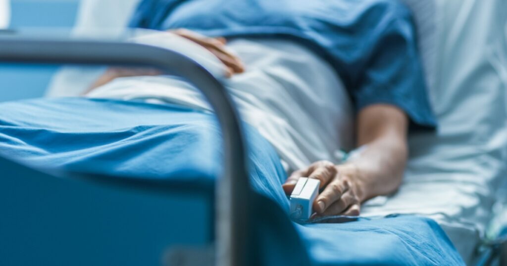 In the Hospital Sick Male Patient Sleeps on the Bed. Heart Rate Monitor Equipment is on His Finger.
