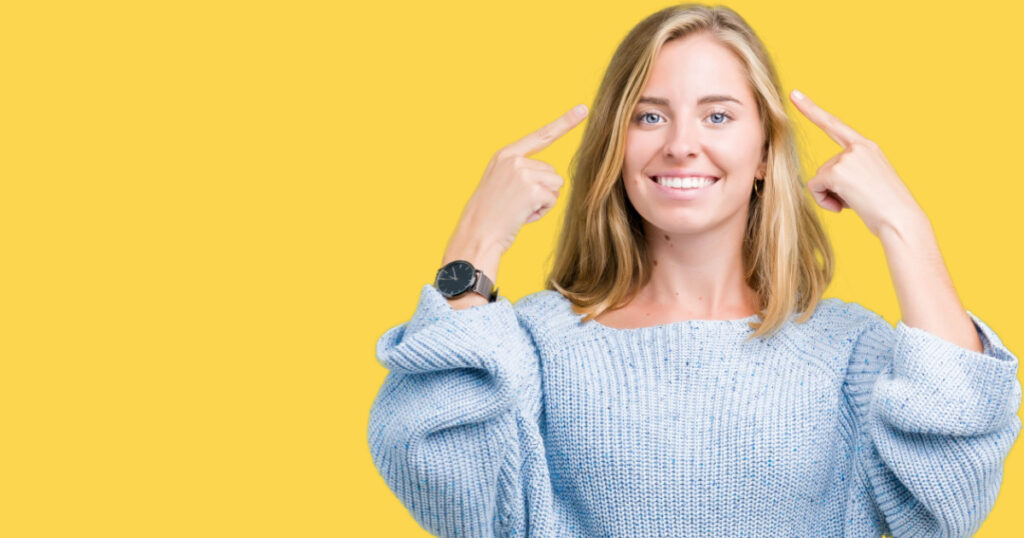 Beautiful young woman wearing blue sweater over isolated background Smiling pointing to head with both hands finger, great idea or thought, good memory
