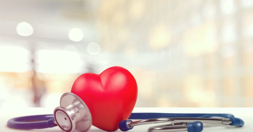 One single alone red heart love shape hand exercise ball with bandage MD medical doctor physician's stethoscope white wood background: Hospital life insurance concept: World heart health day idea