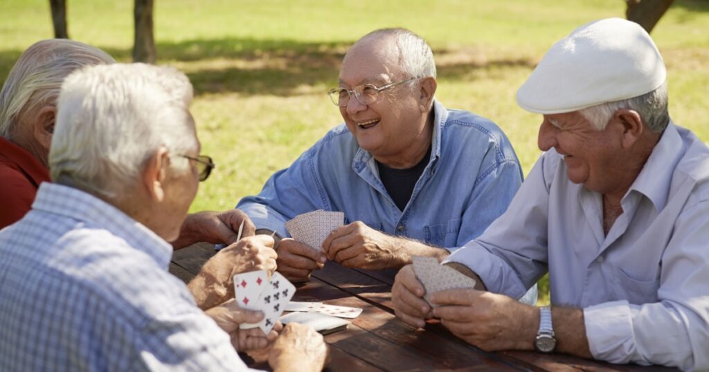 Active retirement, old people and seniors free time, group of four elderly men having fun and playing cards game at park. Waist up