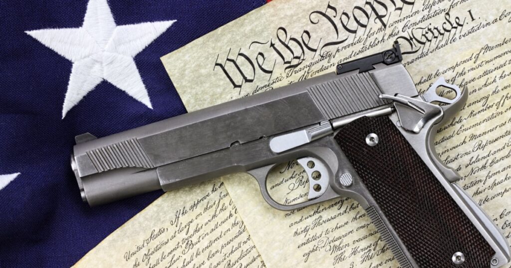 Handgun lying over a copy of the United States constitution and the American flag.
