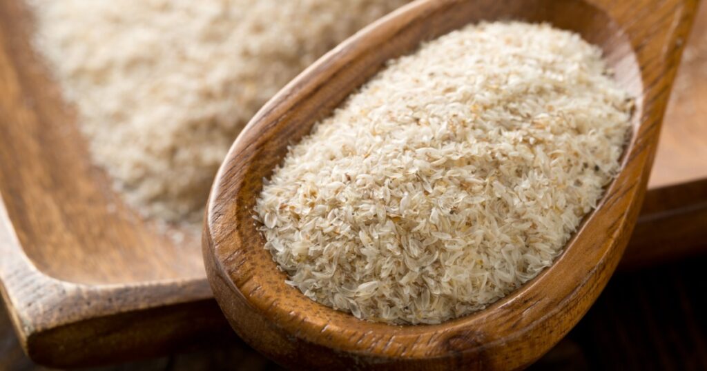 Heap of psyllium husk in wooden spoon and bowl on table. Psyllium husk also called isabgol is fiber derived from the seeds of Plantago ovata plant found in India. Selective focus.