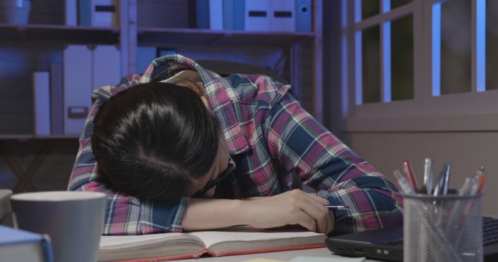 Tired student sleeping on book in dark room at home in midnight. Exhausted of studying girl napping while reading tutorial material. college lady in glasses resting on table stay up late fell asleep.
