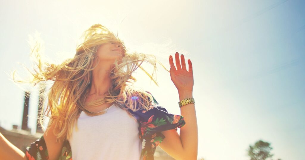 Attractive happy young woman in white t shirt flying hair enjoying her free time at sunset outdoor. Beauty blonde girl portrait at summer. Freedom lifestyle springtime concept. Sun glow on background