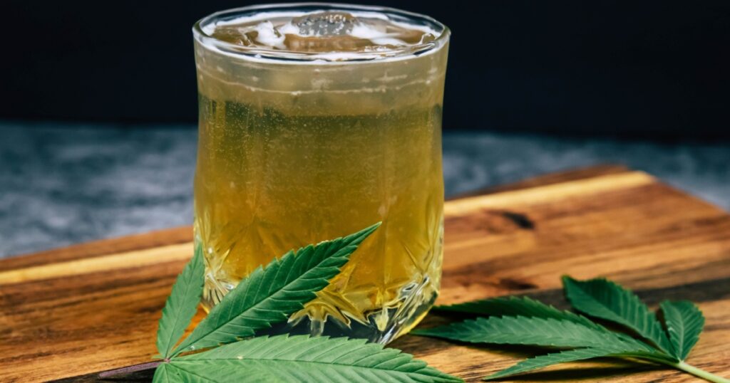 Ice cold Marijuana cannabis infused drink in a crystal clear glass with weed leaves on a dark wood background