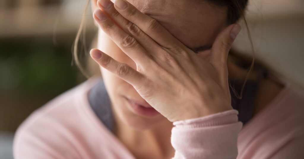 Sad tired young woman touching forehead having headache migraine or depression, upset frustrated girl troubled with problem feel stressed cover crying face with hand suffer from grief sorrow concept