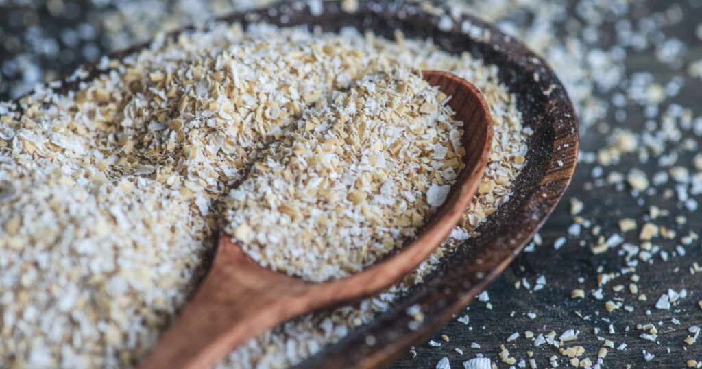 Healthy food concept with oats bran in a bowl with wooden spoon on dark rustic background with copyspace