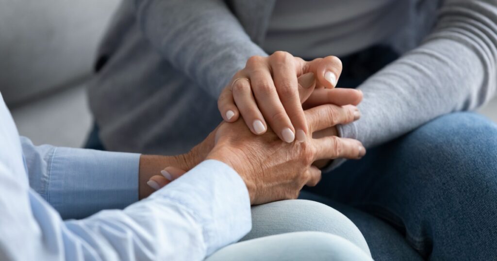 Young woman granddaughter daughter hold old female hand of mother grandma sit on sofa, two women generation help support concept, senior people parents grandparents care and comfort, close up view