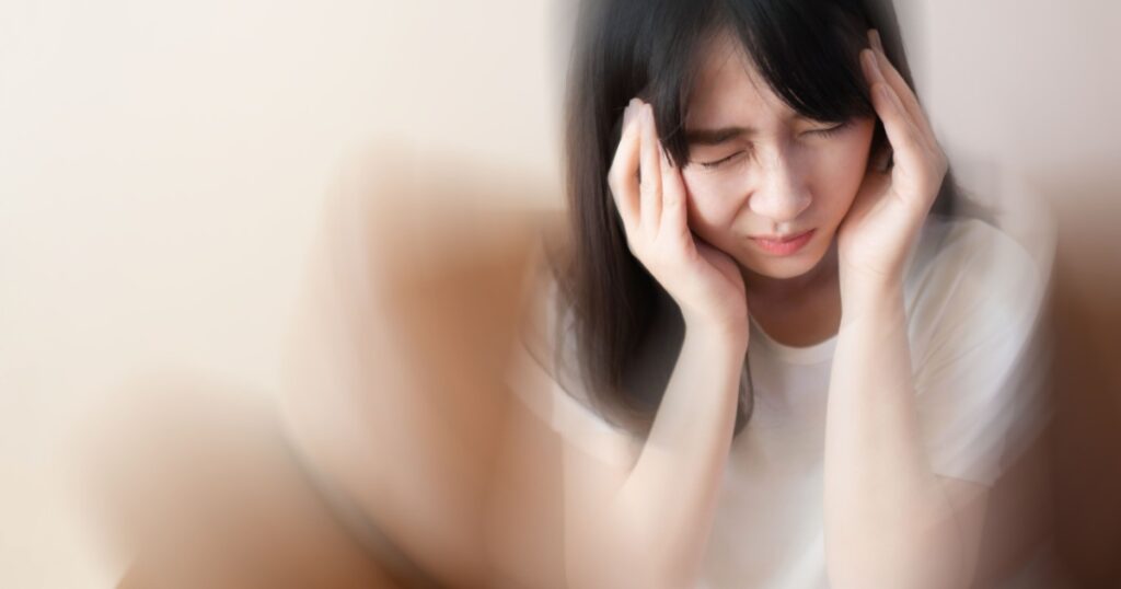 Young female suffering from dizziness, vertigo, headache while sitting on couch at home. Cause of dizzy inclued migraine, stress, stroke, BPPV, Meniere’s disease or brain tumor. Health care