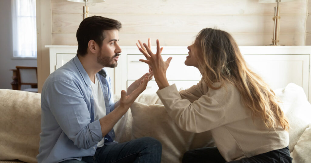 Emotional annoyed stressed couple sitting on couch, arguing at home. Angry irritated nervous woman man shouting at each other, figuring out relations, feeling outraged, relationship problems concept.