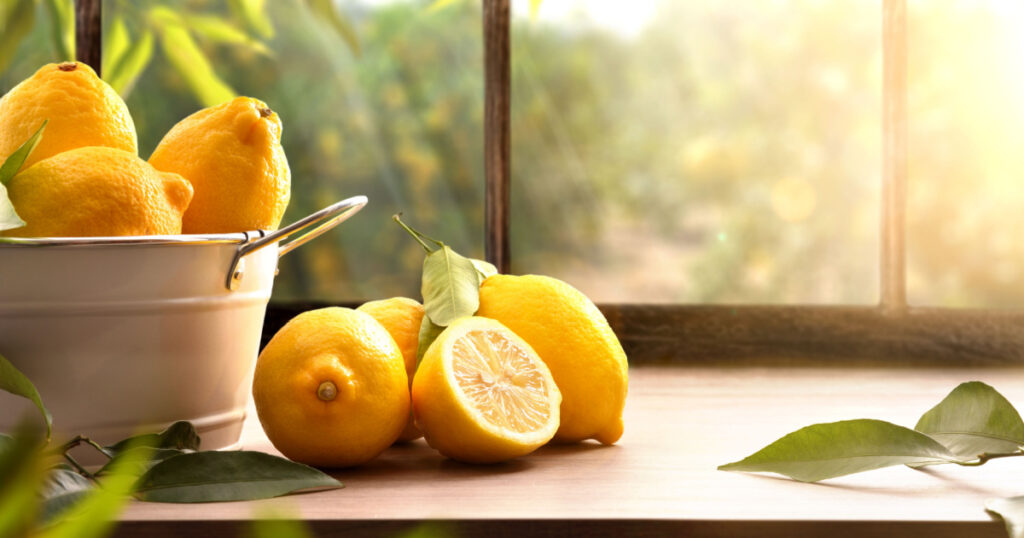 Basket full of lemons on kitchen with a window and a lemon grove in the background. Front view. Horizontal composition.