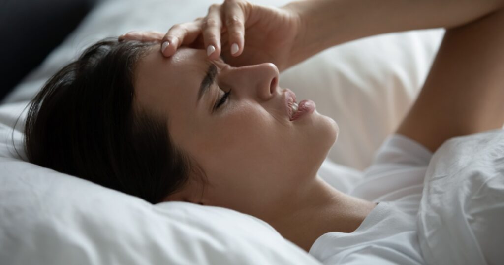 Headache attack. Sad frustrated millennial female spending time in bed lying in pillows touching forehead suffering from migraine fever insomnia feeling ill sick unhealthy waking up after bad dream