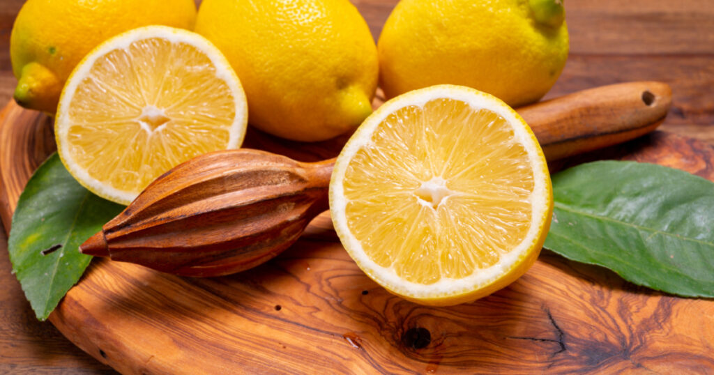 Fresh ripe yellow Italian lemons and wooden juice squeezer, new harvest, on olive tree wood background