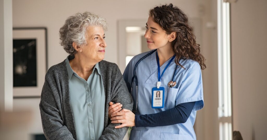 Young caregiver helping senior woman walking. Nurse assisting her old woman patient at nursing home. Senior woman with walking stick being helped by nurse at home.