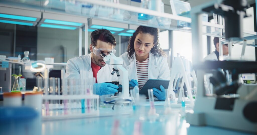 Modern Medical Research Laboratory: Portrait of Latin and Black Young Scientists Using Microscope, Digital Tablet, Doing Sample Analysis, Talking. Diverse Team of Specialists work in Advanced Lab