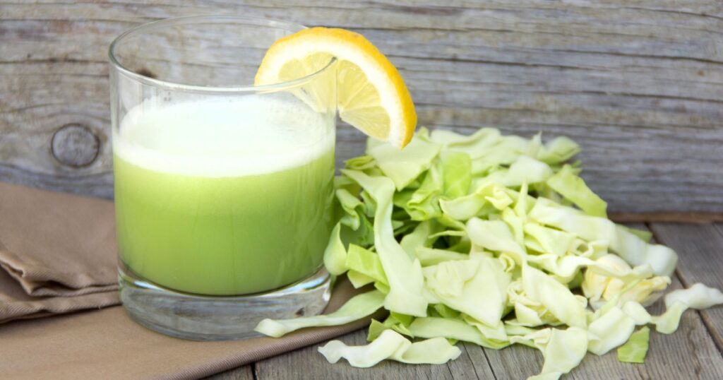 Homemade cabbage smoothie juice in a glass near fresh green chopped cabbage close up on a wooden table. Healthy eating and home cooking concepts