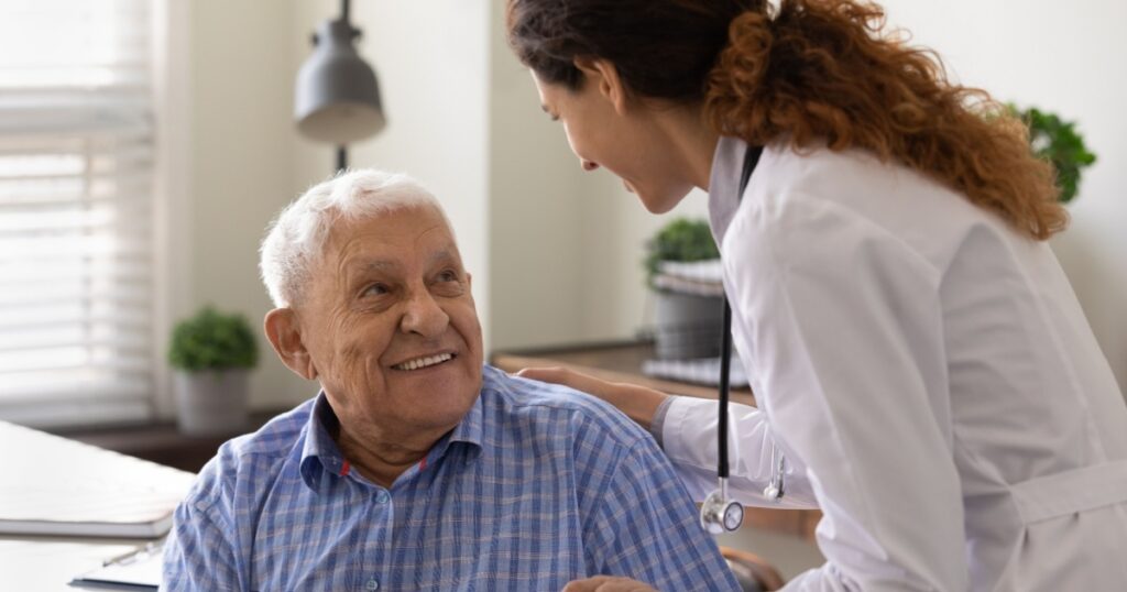 Close up caring nurse holding smiling mature patient hand at meeting in hospital, doctor caregiver wearing uniform comforting and supporting senior man, good news about treatment, empathy and care